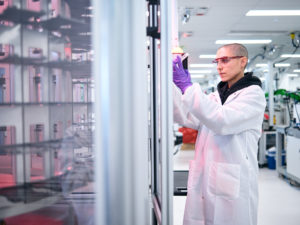 A photo of a Bioworker standing near high throughput automation inspecting a plate of samples