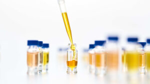 An array of small product vials containing a yellowish oily substance, the center vial in the frame is being pipetted
